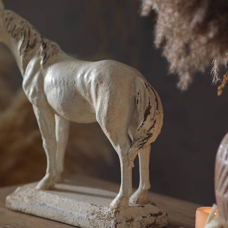 A close-up of the Rustic Horse Sculpture by Vagabond Vintage, its weathered white finish and detailed tail on a rectangular base bring antique charm to a wooden surface in soft light.