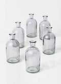 Six empty Smoke Medicine Bottle Bud Vases by Jamali Garden are arranged in a loose circle on a white surface, each casting faint shadows.