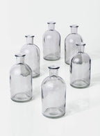 Six empty Smoke Medicine Bottle Bud Vases by Jamali Garden are arranged in a loose circle on a white surface, each casting faint shadows.