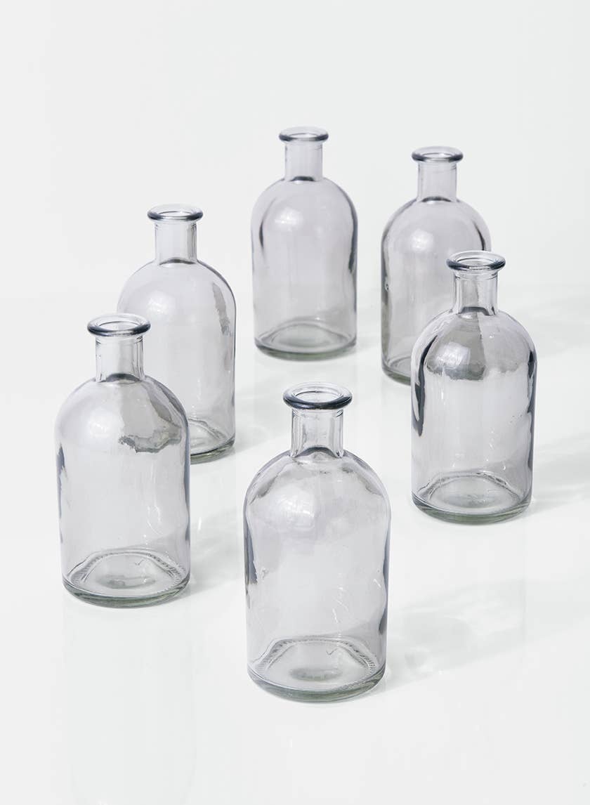 Six empty Smoke Medicine Bottle Bud Vases by Jamali Garden are arranged in a loose circle on a white surface, each casting faint shadows.