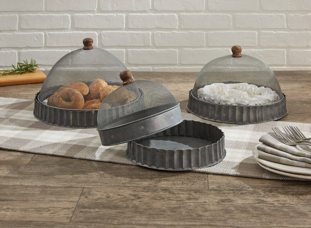 The Park Designs Covington Screen Covers with Bases, set of 3, feature metal mesh and wooden handles on a checkered runner; one is lifted to reveal baked goods while others shield pastries. Plates and forks are stacked nearby. Hand wash for best care.