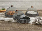 The Park Designs Covington Screen Covers with Bases, set of 3, feature metal mesh and wooden handles on a checkered runner; one is lifted to reveal baked goods while others shield pastries. Plates and forks are stacked nearby. Hand wash for best care.