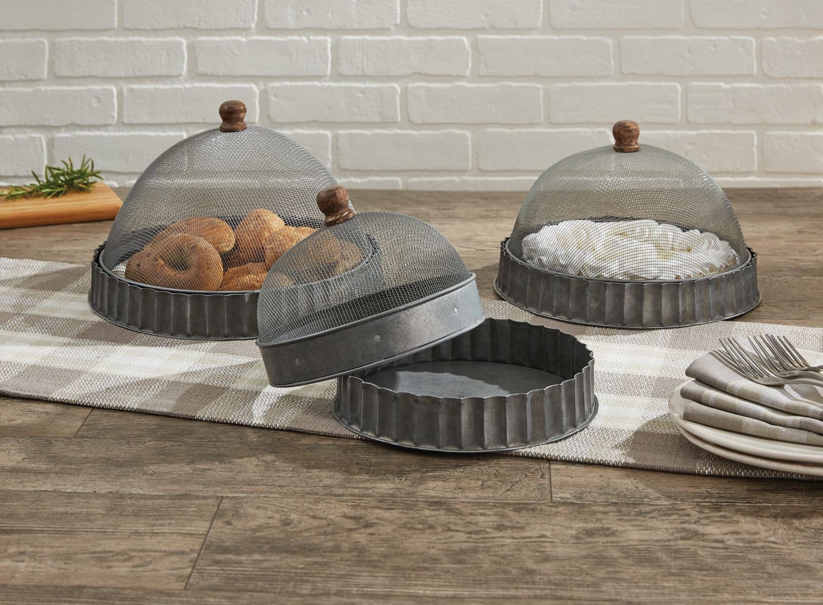 The Park Designs Covington Screen Covers with Bases, set of 3, feature metal mesh and wooden handles on a checkered runner; one is lifted to reveal baked goods while others shield pastries. Plates and forks are stacked nearby. Hand wash for best care.