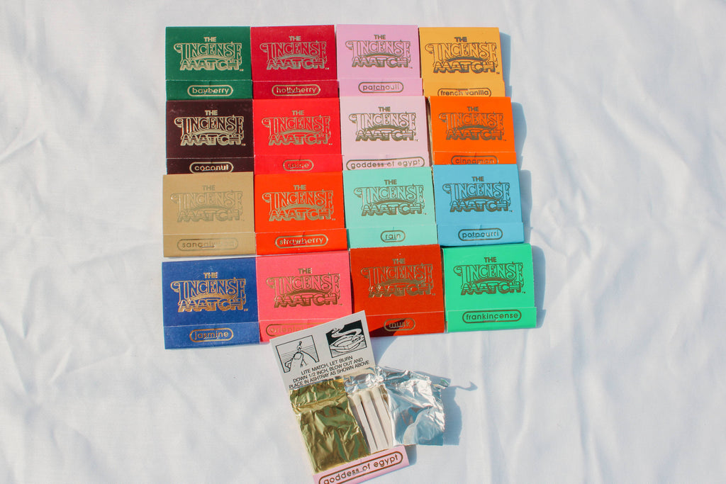 A set of colorful Fragrance Matches by H&L NOVELTIES INC, each handcrafted matchbook features a unique label and hue, arranged neatly with a match pack and silver pouch—perfect as a stylish bathroom accessory.