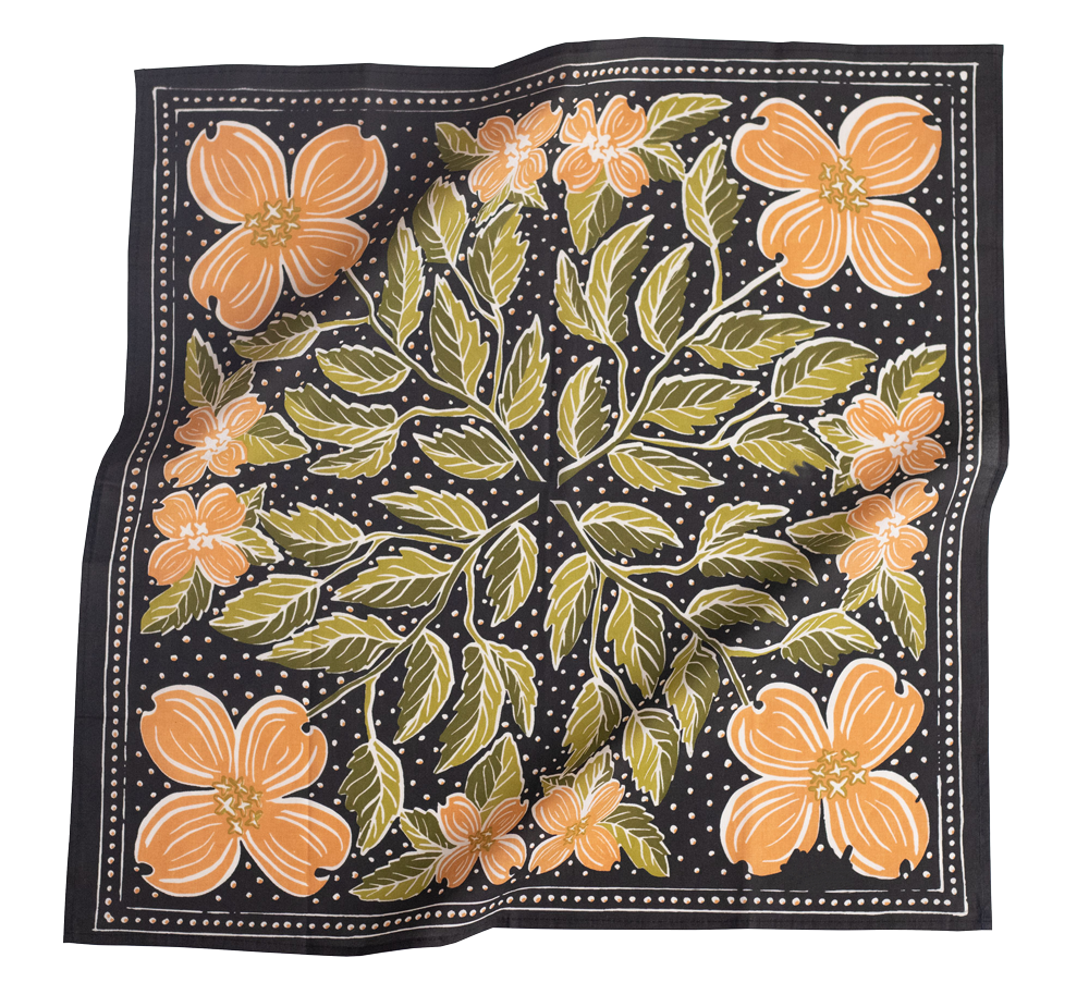 The No. 046 Amy Bandana by Handker Bandanas is a square black cotton scarf, hand screen-printed with large orange dogwood flowers, green leaves, and small white dots in a decorative symmetrical design. The fabric has a slightly wrinkled look.