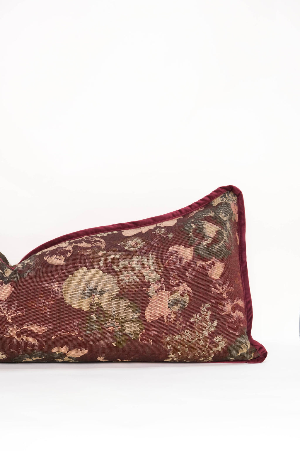 The Tapestry Long Lumbar by Twenty Third by Deanne is a rectangular maroon jacquard pillow with a floral pattern in muted greens, pinks, and beige, finished with maroon piping and shown on a plain white background.