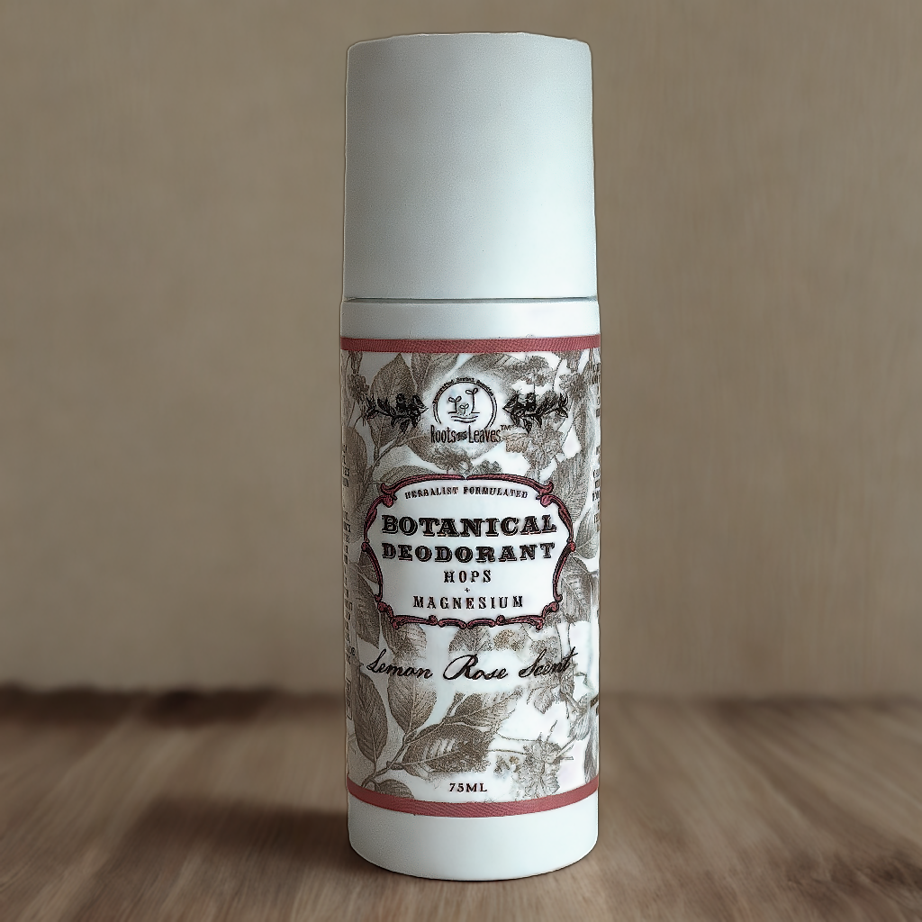 A white cylindrical bottle of Roots And Leaves Botanical Magnesium Deodorant with a vintage floral label, featuring Lemon Rose Scent and notes like hops and baking soda free, sits on a wooden surface.