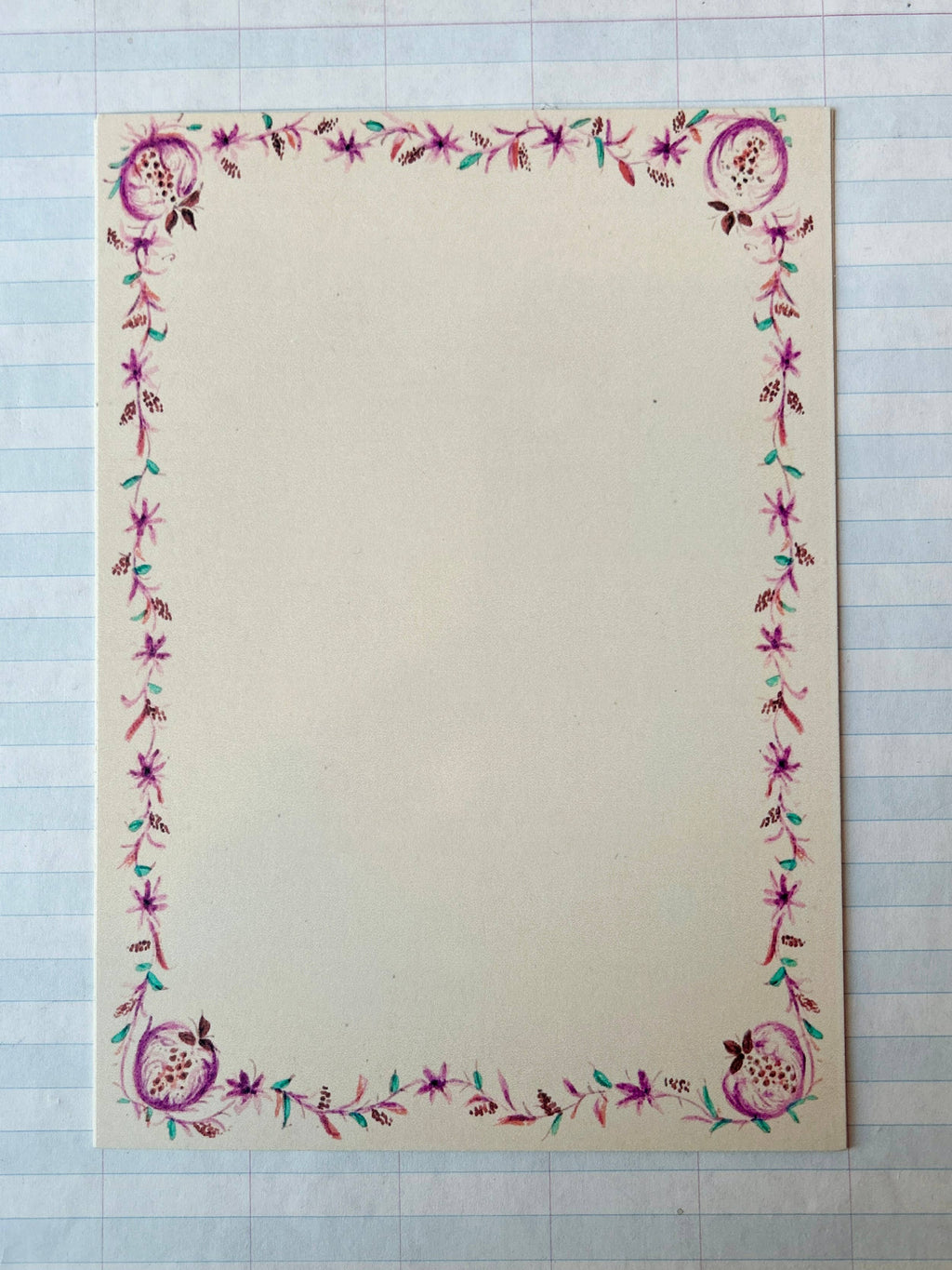 A creamy white card from Parcel's French Menu Stationery Set II: 2 features a pink and purple floral border with green leaves, displayed on graph paper. The elegant set includes 8 printed cards.