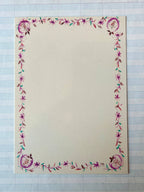 A creamy white card from Parcel's French Menu Stationery Set II: 2 features a pink and purple floral border with green leaves, displayed on graph paper. The elegant set includes 8 printed cards.
