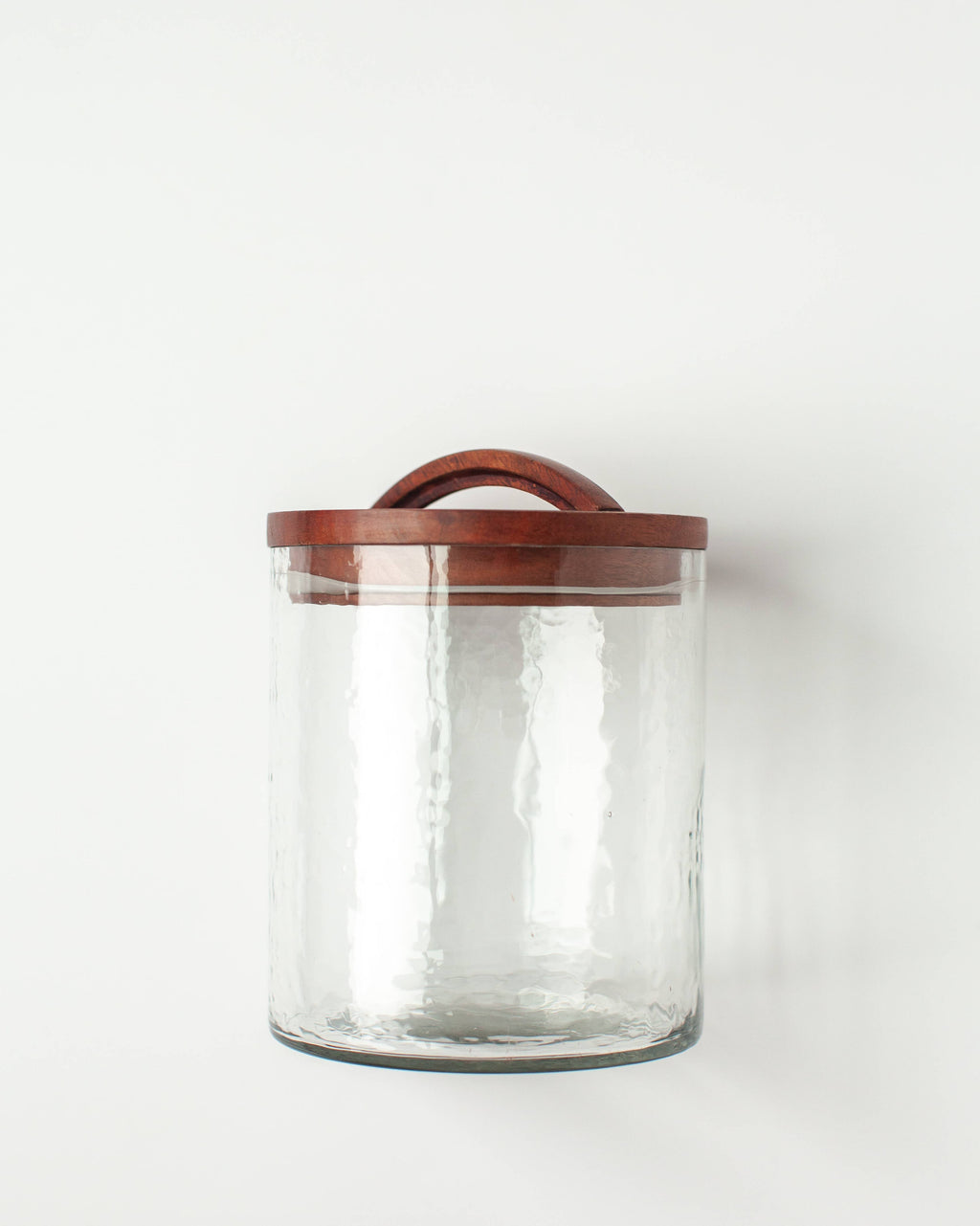 The Handblown Hammered Glass Canisters: Smoke / Small by Creative Women features recycled glass with a textured finish and a hand-carved wooden lid with a curved handle, shown on a plain white background.