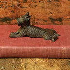 A HomArt Terrier Door Wedge, Cast Iron - Antique Brown, sits atop a closed red hardcover book against a rustic wooden background.
