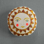 The Skippy Cotton Bright Neon Sun Pillow is a handmade, cotton-filled cushion featuring a stylized sun face with blue eyes, pink cheeks, and a vibrant yellow and red sunburst—perfect for whimsical home decor.
