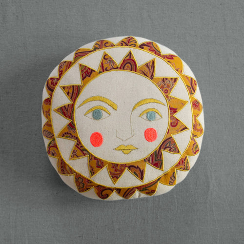 The Skippy Cotton Bright Neon Sun Pillow is a handmade, cotton-filled cushion featuring a stylized sun face with blue eyes, pink cheeks, and a vibrant yellow and red sunburst—perfect for whimsical home decor.