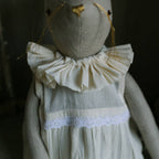The Skippy Cotton Ruffle Bun Ragdoll is a handmade linen rabbit doll with long thread whiskers, hand-stitched details, and a ruffled cream cotton dress with lace trim, set against a neutral background.