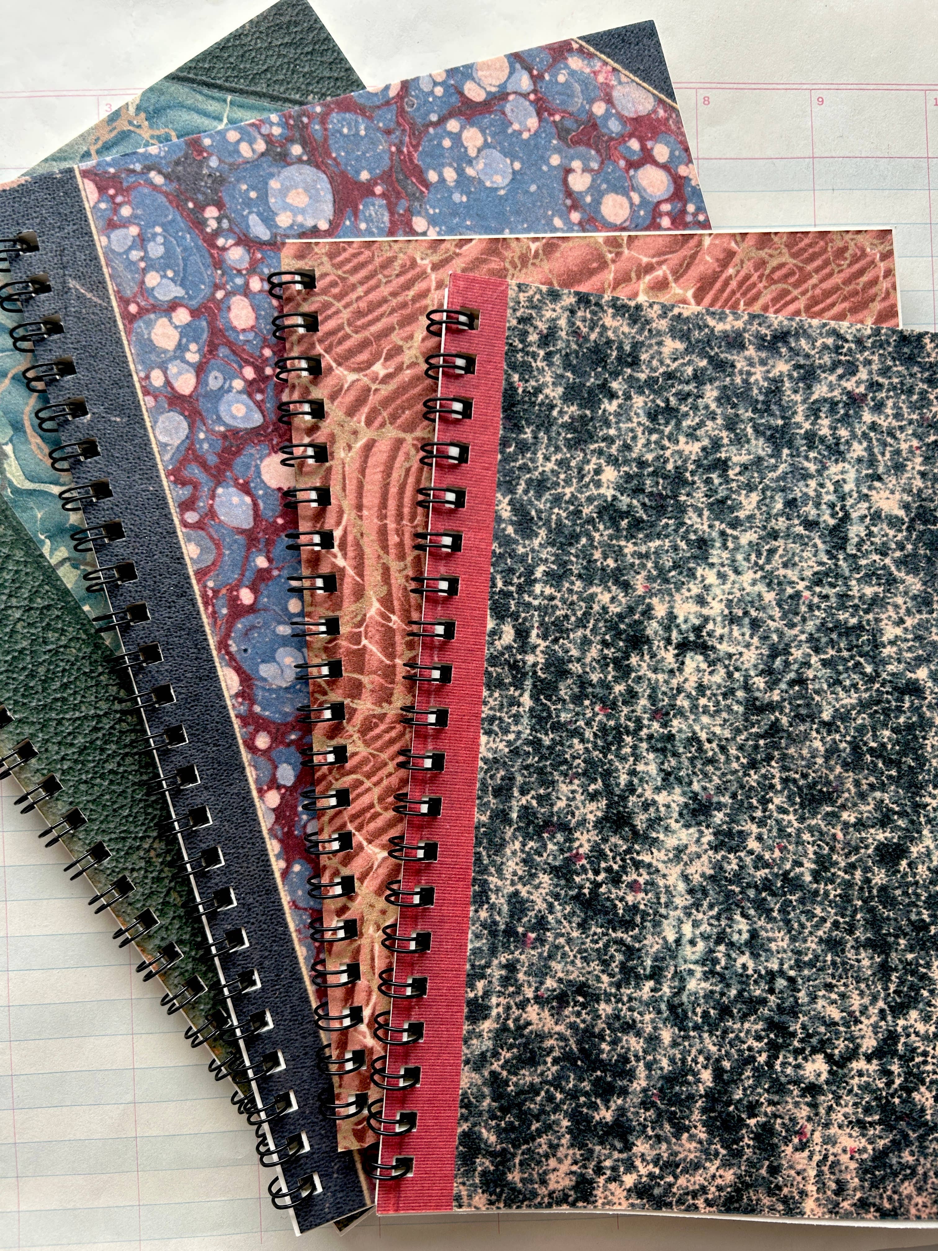 Four Parcel Antique Endpaper Notebooks (Small, Composition, Unlined) with vintage marbled and textured covers in assorted colors and patterns are stacked atop lined paper.
