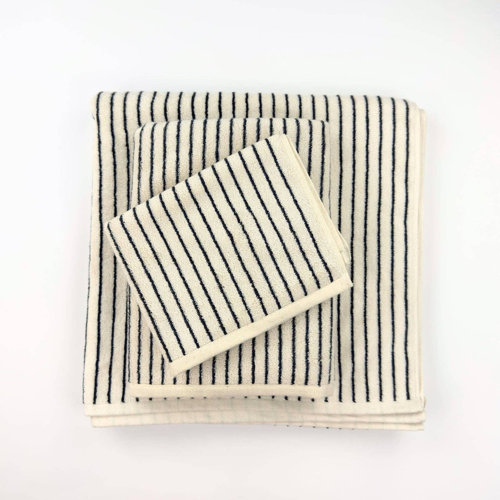 Three Turkish Cotton Striped Terry Towels by The Loomia, each a different size, are stacked from largest to smallest on a white surface; they feature thin, evenly spaced black stripes and are neatly folded.