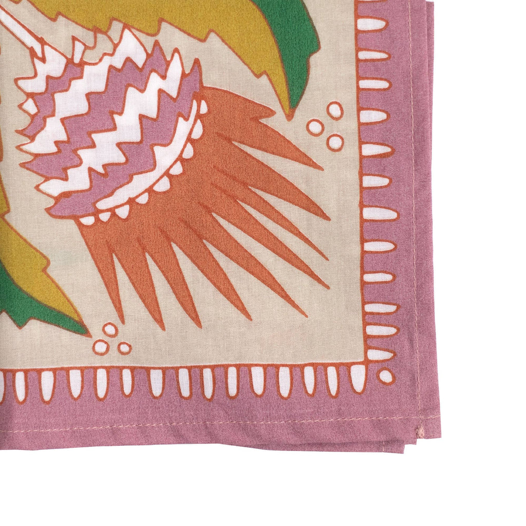 A close-up of the No. 081 Martha Bandana by Handker Bandanas, featuring premium cotton, a pink border, and a vibrant abstract design with spiky orange and white details alongside green plant-like shapes.