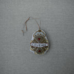 The Skippy Cotton Courage Crest Token is a gold, white, and red embellished ornament with "COURAGE" across the center, hanging by a loop—perfect for evoking Oz spirit along the Red Brick Road.