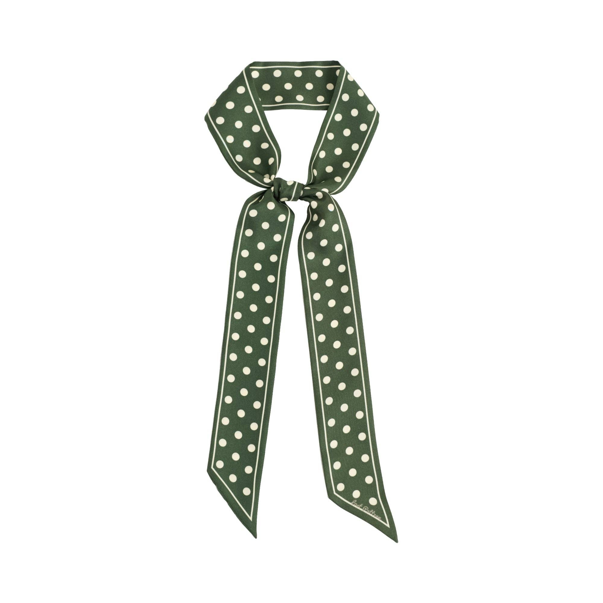 The Silk Skinny Scarf in Dark Green by Lost Pattern NYC features a white border and polka dots, styled with a loose knot and long ends.