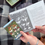 A person holds a tarot card from the Tarot of the Woodland Wardens by Jessica Roux, published by Simon & Schuster, showcasing frogs in cups alongside a corresponding illustration and description in the 224-page English guidebook. The scene is set atop a checkered blanket with additional nature-themed cards and the product box nearby.