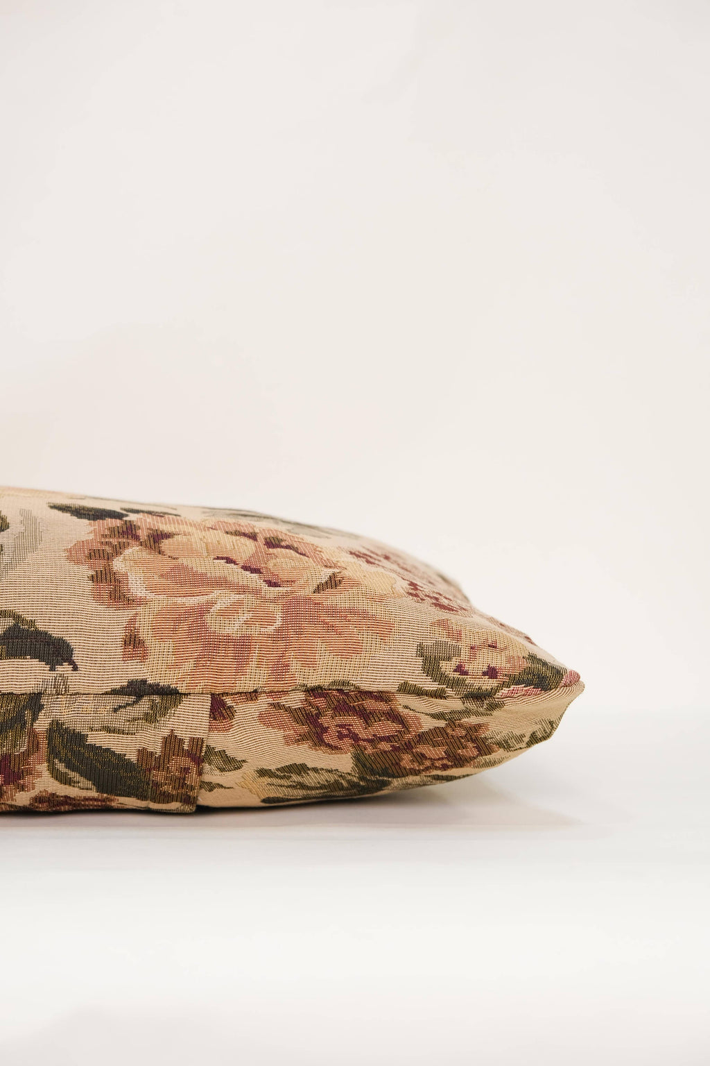 The Tapestry Long Lumbar pillow by Twenty Third by Deanne, featuring a reversible floral pattern in beige, pink, and green, rests on a white surface against a plain light background.