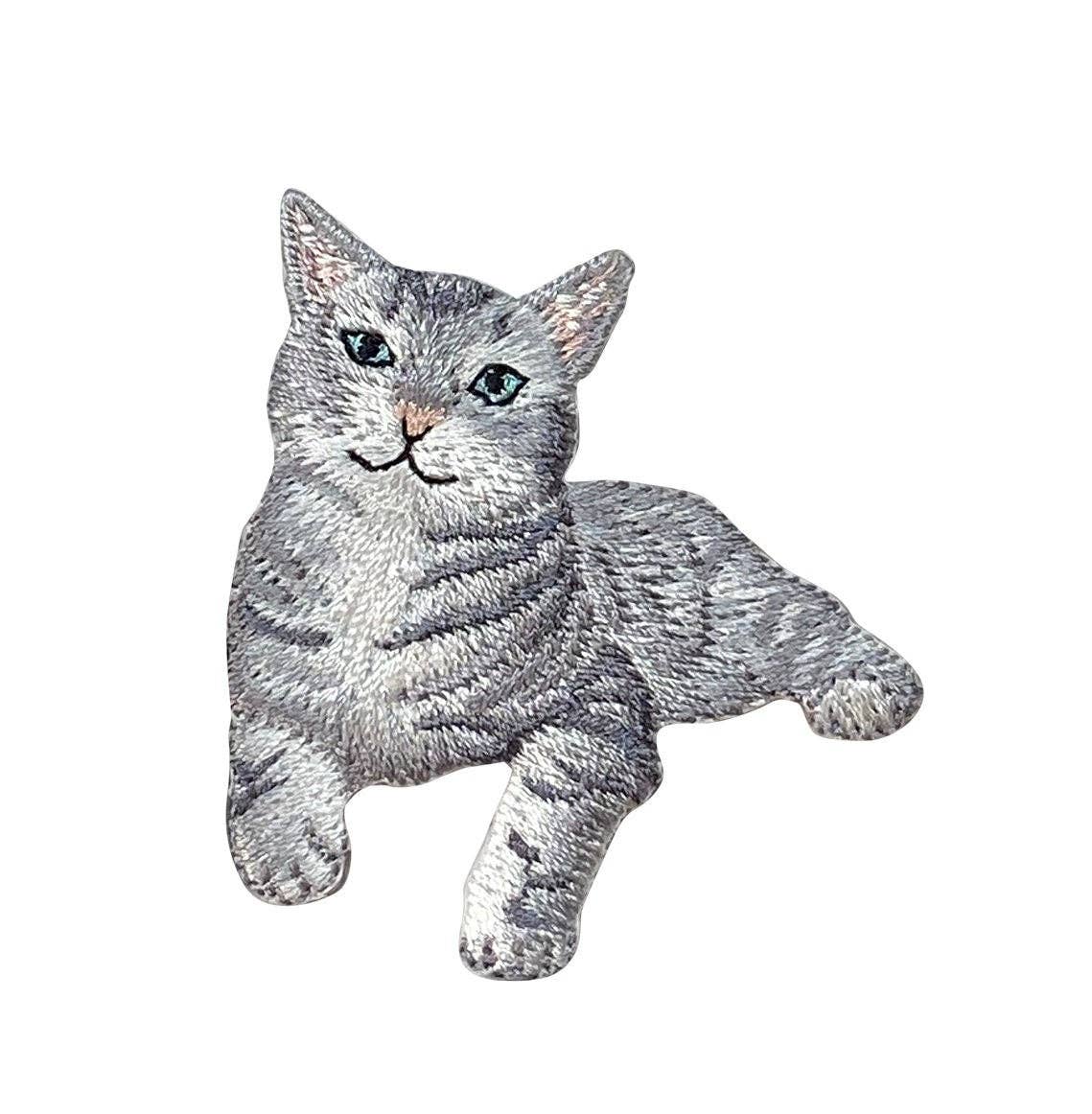 The Gray Tabby Cat Iron on Patch by Wholesale Applique features a lying gray tabby kitten with green eyes, perfect for customizing jackets or bags. Ideal for cat lovers and pet-themed projects.