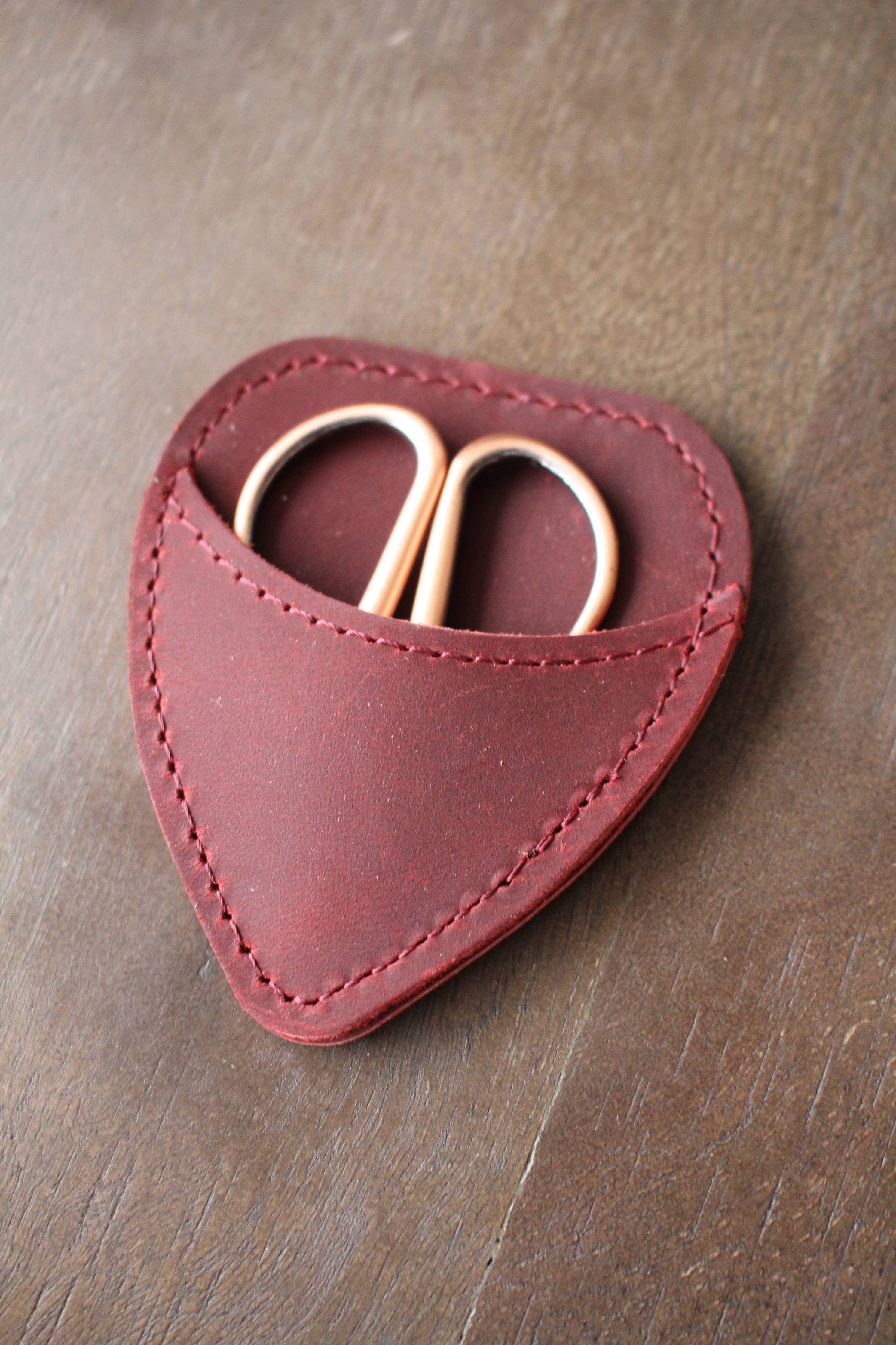 The NNK Press Mini Scissor Keepers: Chestnut features gold-handled embroidery scissors in a maroon, guitar-pick-shaped leather pouch—compact and ideal for your knitting bag.