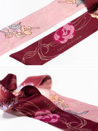 A close-up of the Lost Pattern NYC Silk Skinny Scarf - Ruby Red, featuring floral patterns in pink, burgundy, and gold tones with "LOST PATTERN" printed on the burgundy section. Ideal as a stylish hair accessory or headband.