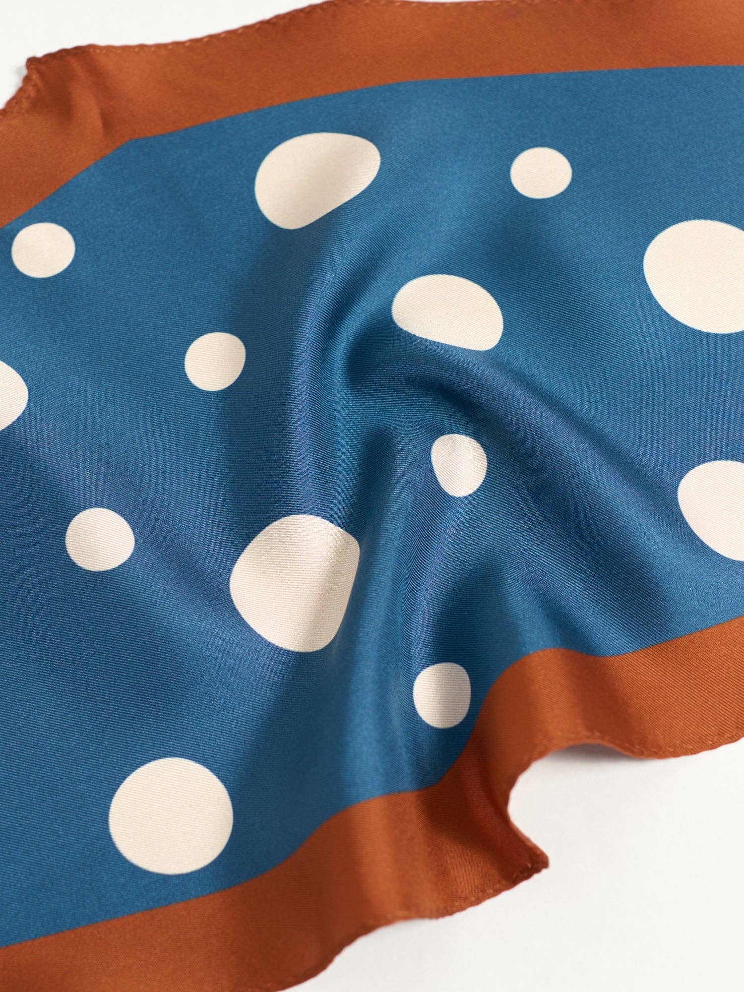 The Lost Pattern NYC Silk Polka Dot Diamond Neckerchief in Salted Caramel features a diamond shape, white polka dots, a wide agate grey border, and a softly crinkled finish.