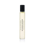A clear glass Heretic Parfum SCANDALWOOD ROLLERBALL: 10ML perfume bottle with a black cap stands upright on a white background. The label is printed vertically, suggesting notes of sandalwood and musk.