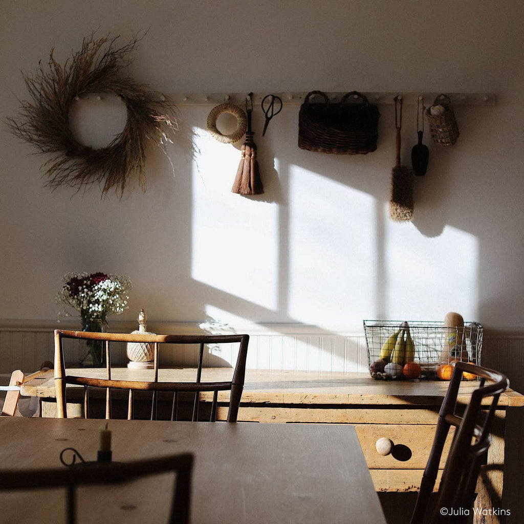 Sunlight streams into a rustic kitchen with wooden tables and chairs. On the counter, Bloomist’s Gardener's Planting Set adds charm, while a wire basket of veggies and gardening tools bring cozy, natural warmth to the space.