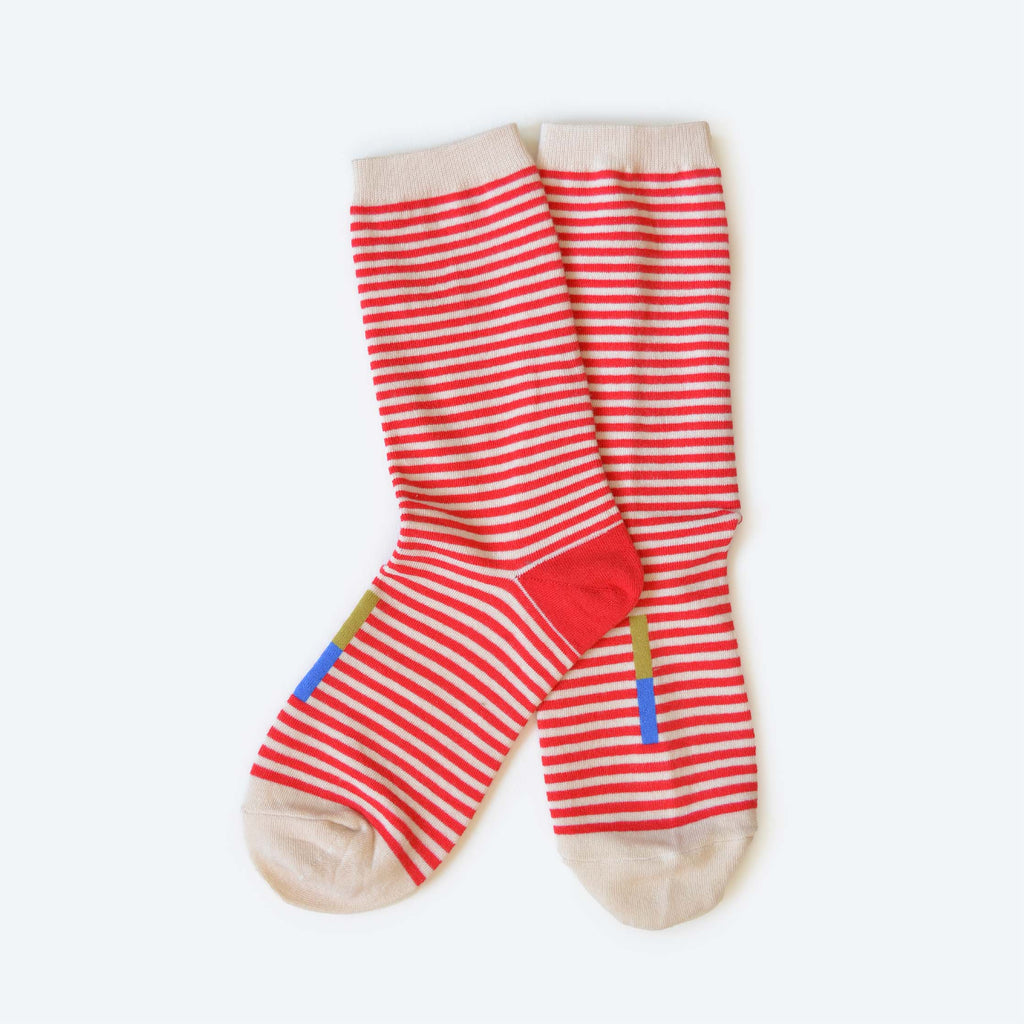The Clayton Sock by Hooray Sock Co. is a unisex crew sock with red and white stripes, cream toes, heels, and cuffs, plus a small blue and yellow rectangle near the ankle. Cotton-spandex blend. Shown laid flat on a white background.
