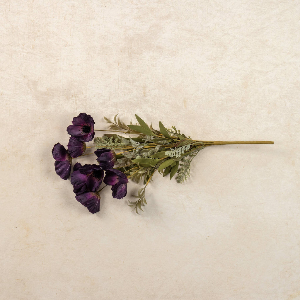 A 22" Artificial Dark Purple Poppy Bush by Ragon House, featuring vibrant blooms and green leaves, is displayed on a light beige textured surface.