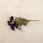 A 22" Artificial Dark Purple Poppy Bush by Ragon House, featuring vibrant blooms and green leaves, is displayed on a light beige textured surface.