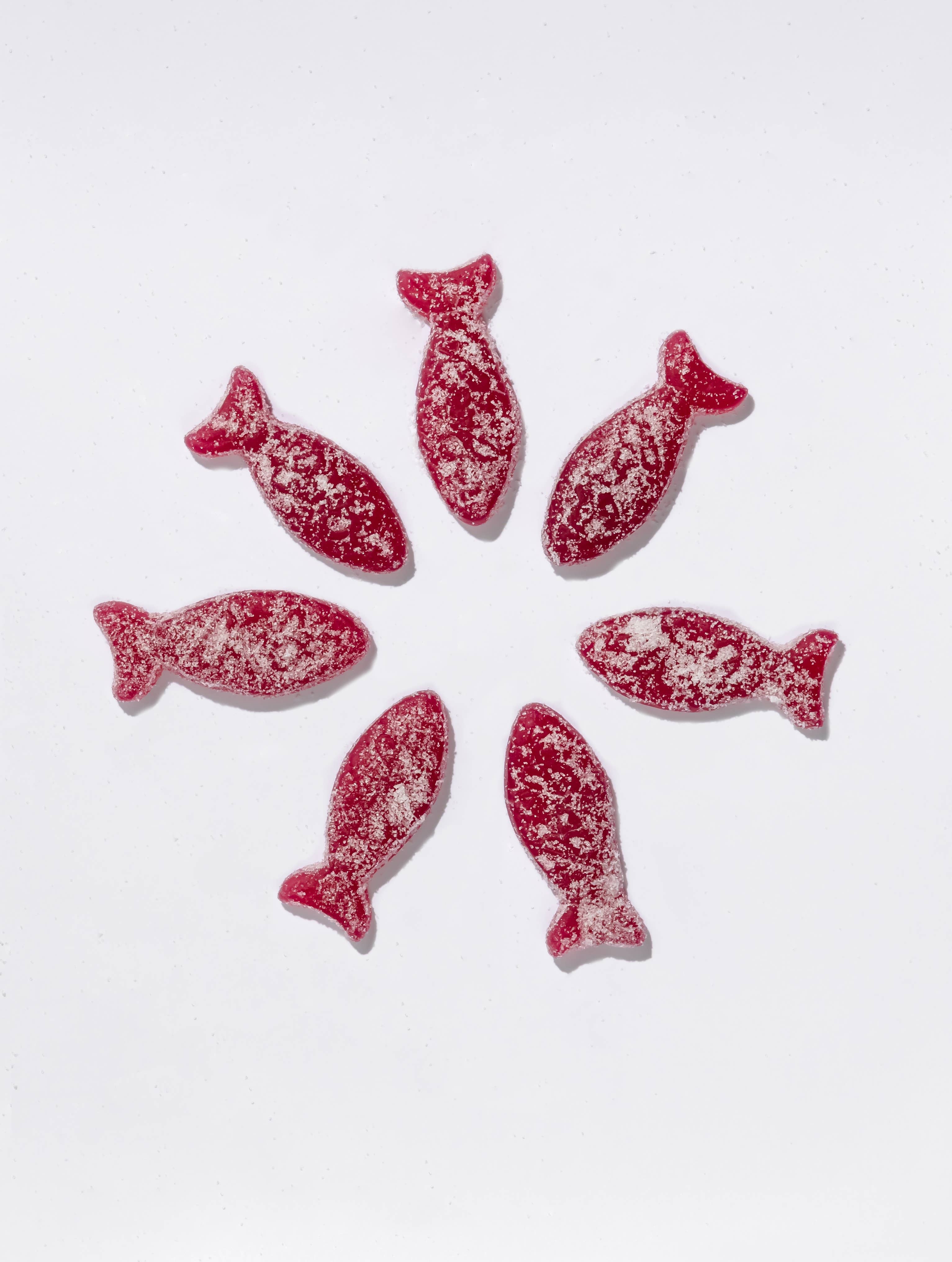 Seven sour blackberry fish candies from BonBon - A Swedish Candy Co are arranged in a circle on a white background.