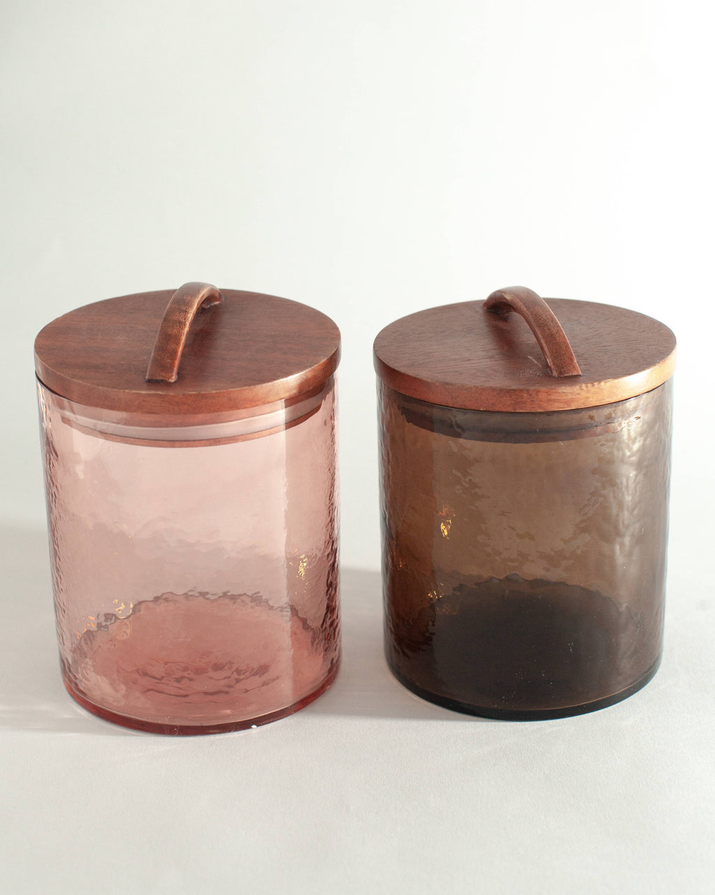 Two Handblown Hammered Glass Canisters: Smoke / Medium by Creative Women, each with a hand-carved wooden lid and curved handle, sit side by side on a light background.