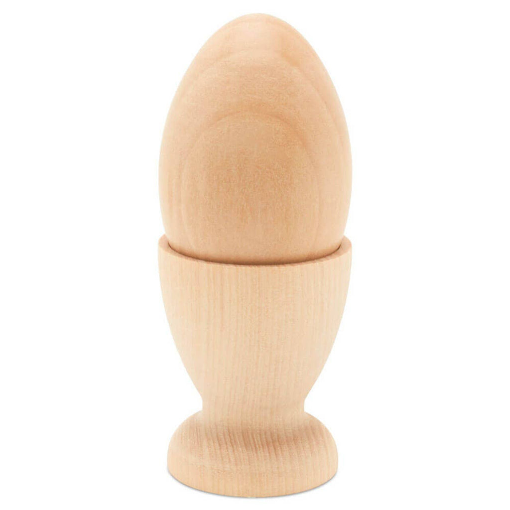 The Wooden Egg Cup Holder by Woodpeckers Crafts displays a smooth, unfinished wooden egg upright in a plain, flat-bottom holder, both with simple designs on a white background.