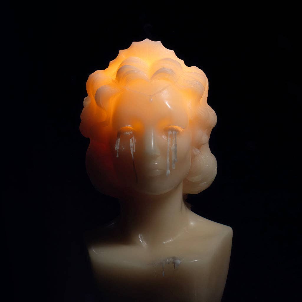Heretic Parfum's WEEPING BUST is a limited edition candle shaped like a woman’s bust, lit from within to let wax drip like tears from her eyes, set against a dark background.