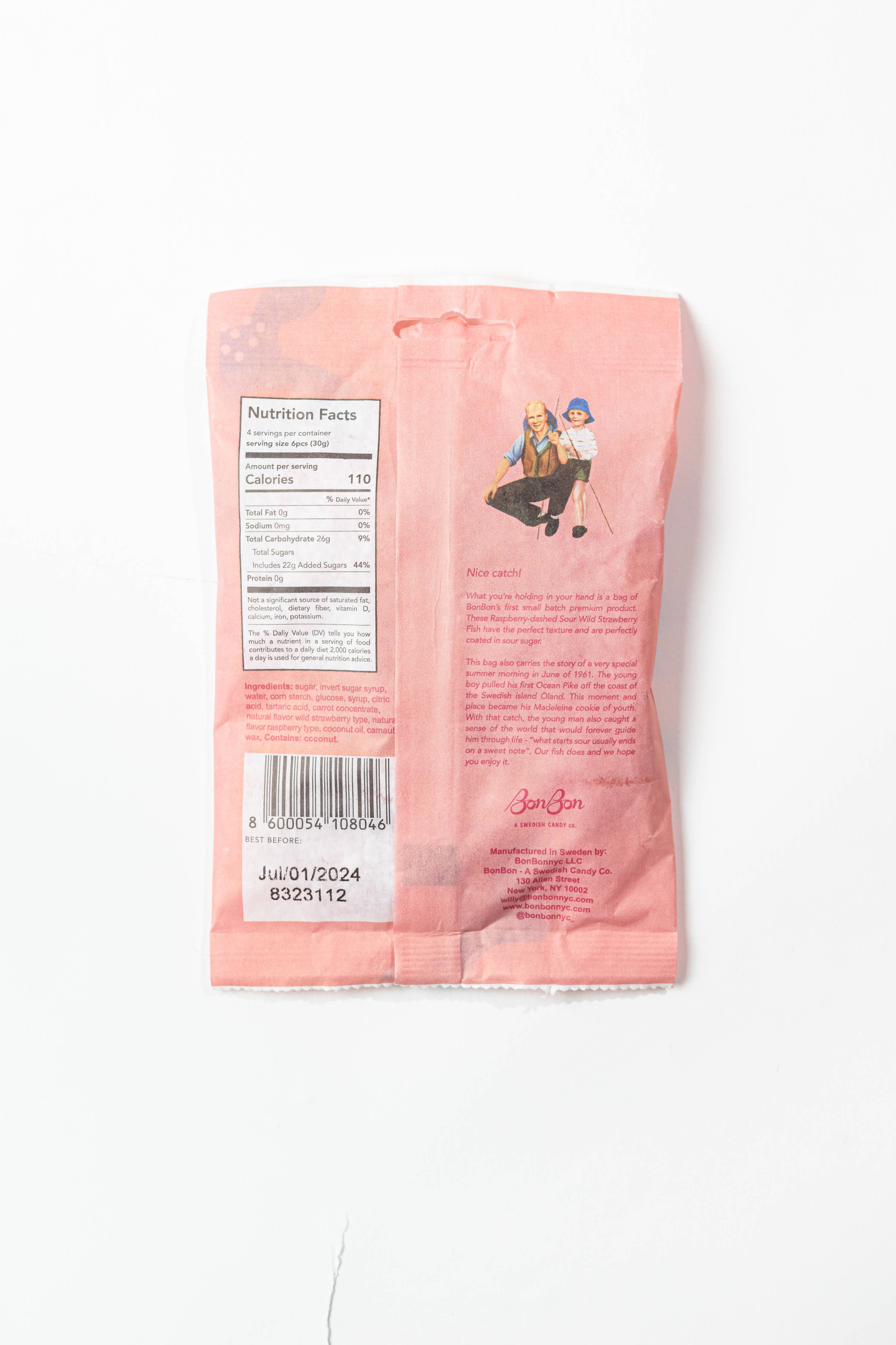 The back of the BonBon - A Swedish Candy Co Sour Wild Strawberry Fish 5.2oz (150g) vegan candy shows a pink package with nutrition facts, barcode, text, and two people sitting together. The expiration date is printed near the bottom.