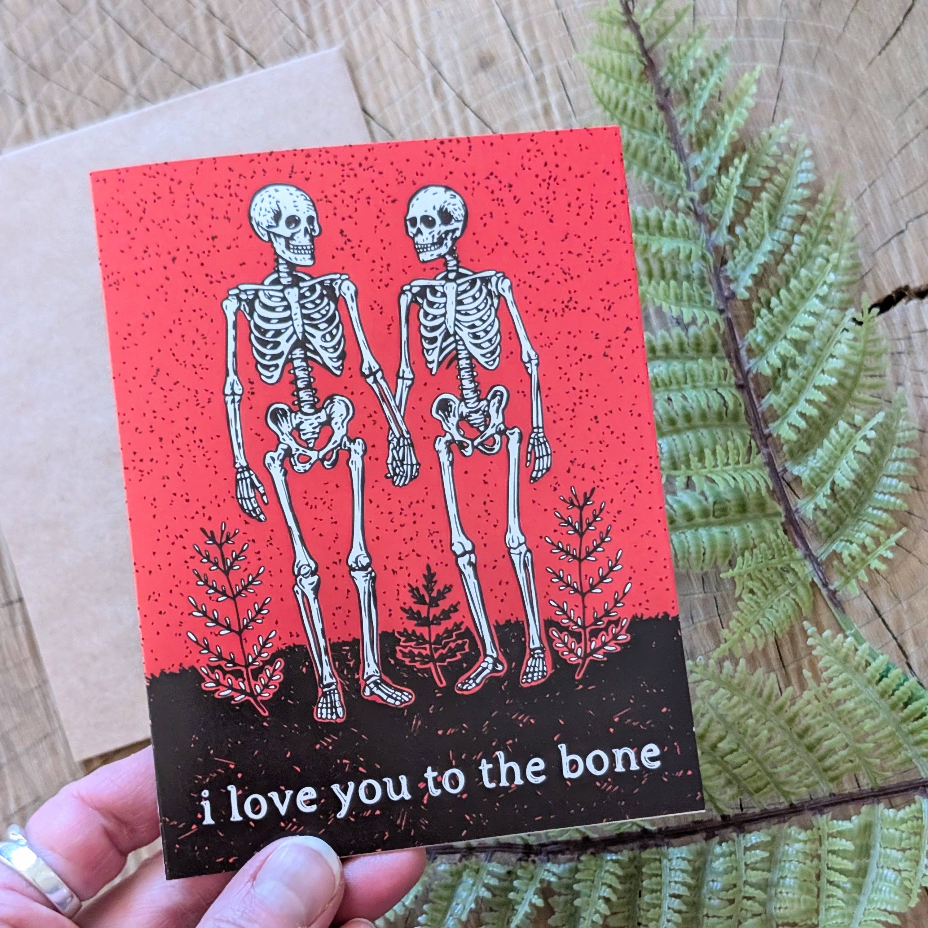 A hand holds the ilikesara "I love you to the bone" greeting card—a skeleton-themed Valentine or Halloween card, perfect for expressing dark romantic love.