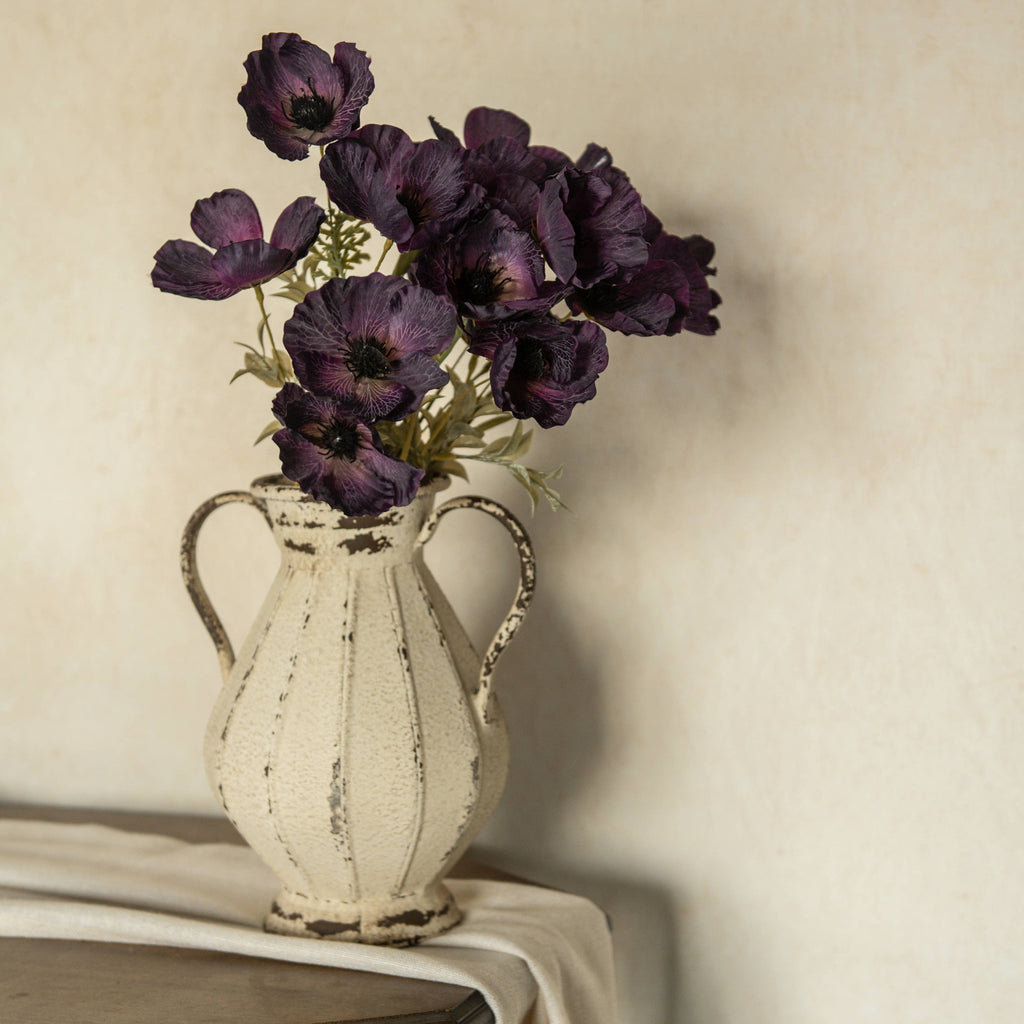 A vintage cream vase holds the 22" Artificial Dark Purple Poppy Bush by Ragon House, displayed on draped fabric with a neutral textured background.