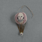The Skippy Cotton "Wonderful Wizard / Balloon" wallhanging ornament features a hand-stitched face with pink hair, ruffled collar, and gold threads on a gray background, creating whimsical embroidered art inspired by Oz.