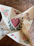 The Parcel Victorian Valentine Puzzle: Romantic sits open on a wooden surface, revealing a heartfelt message in the center, surrounded by painted flowers and birds on creamy white cardstock.