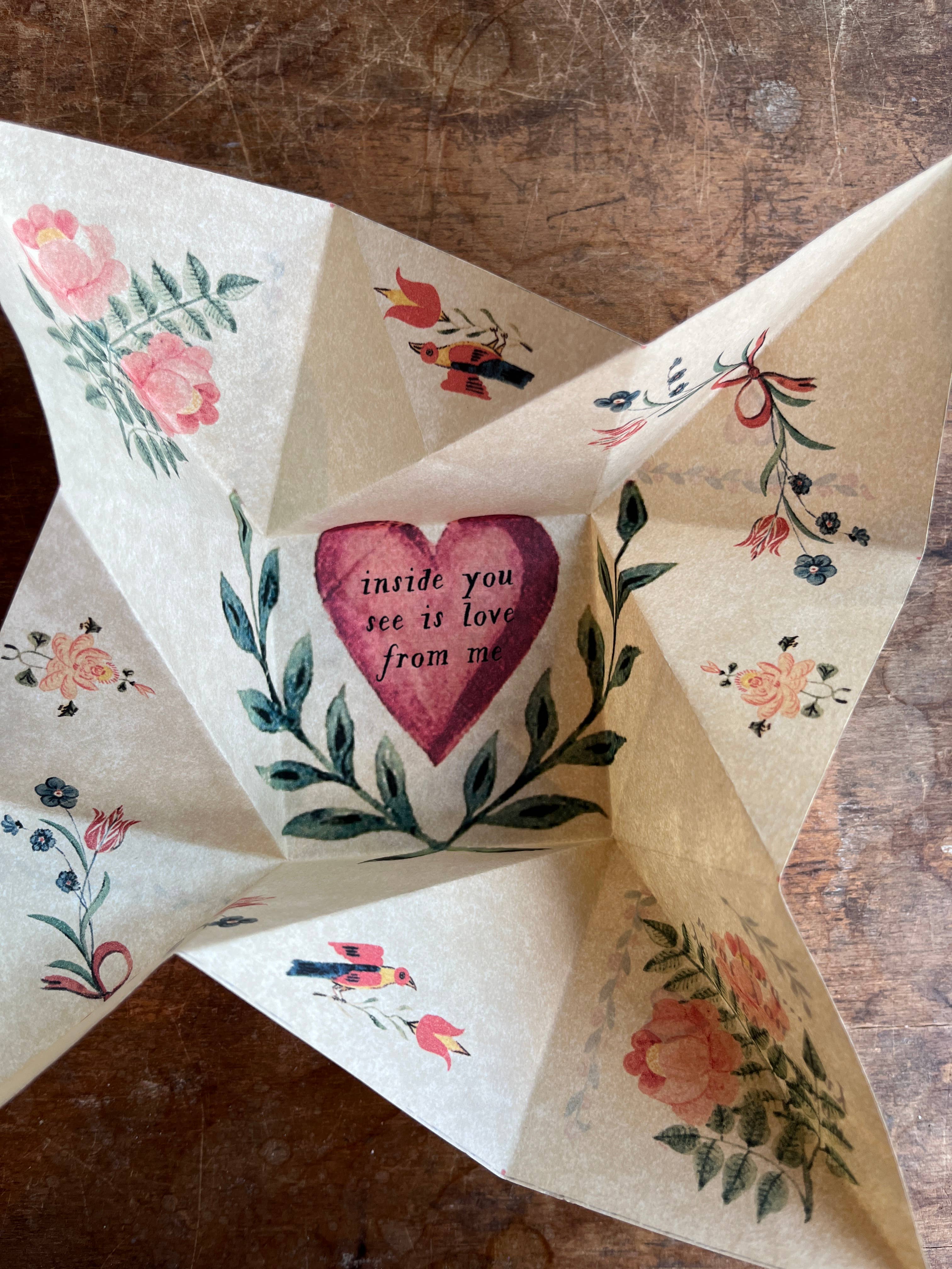 The Parcel Victorian Valentine Puzzle: Romantic sits open on a wooden surface, revealing a heartfelt message in the center, surrounded by painted flowers and birds on creamy white cardstock.