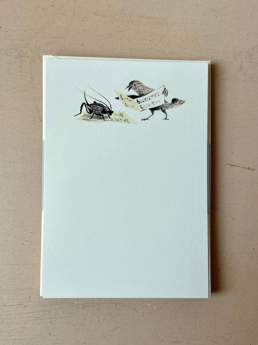 The Music Lessons Mini Stationery Set by Parcel includes 8 creamy white cards, each with a bird and sheet music illustration facing a violin-playing cricket at the top. The rest of the notecard is blank for your message.