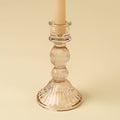 The Indaba Trading Callista Glass Candleholder Large in blush, paired with a beige taper candle, is perfect for vintage-inspired decor and displayed against a light beige background.