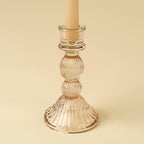 The Indaba Trading Callista Glass Candleholder Large in blush, paired with a beige taper candle, is perfect for vintage-inspired decor and displayed against a light beige background.