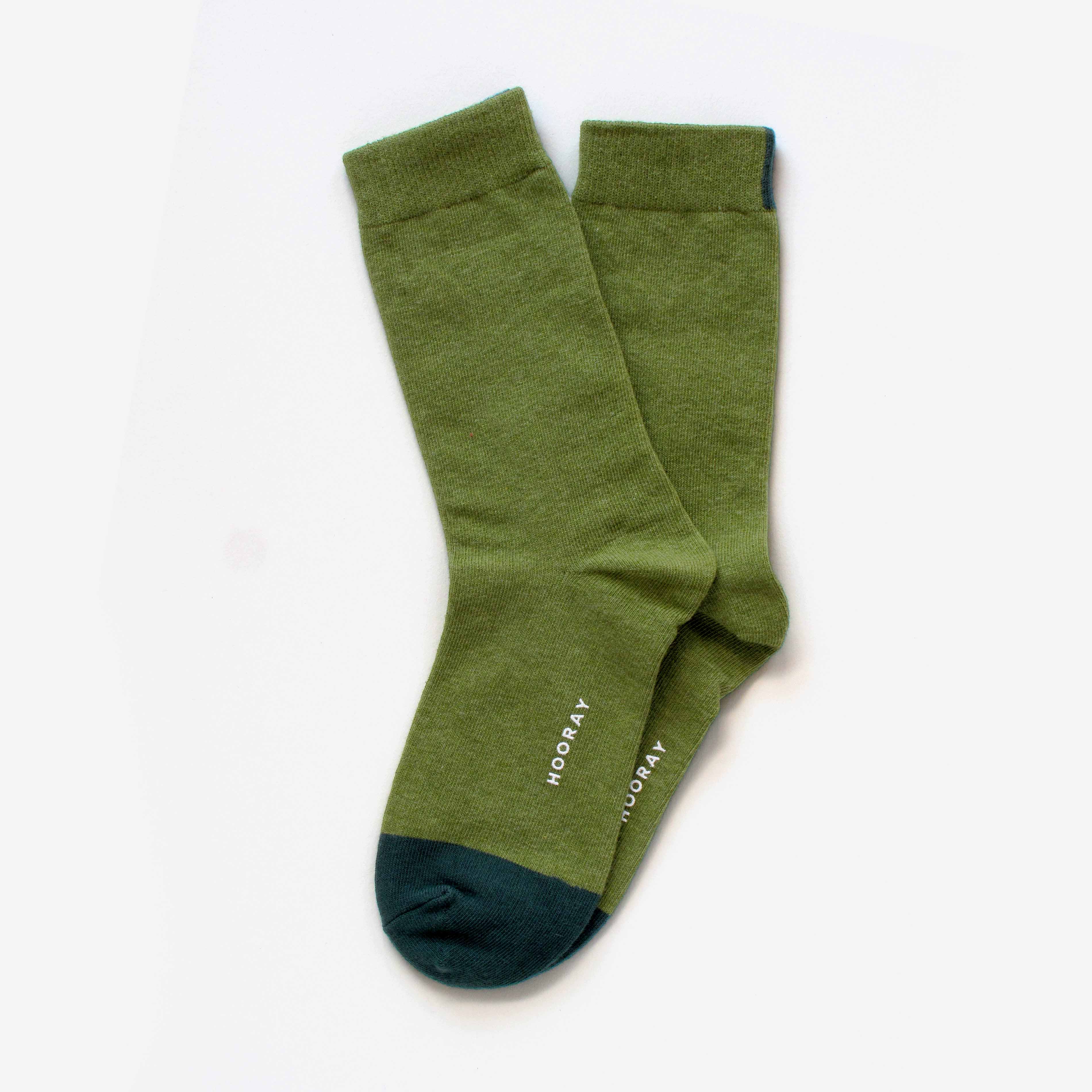A pair of Lafayette Moss Green Crew Socks by Hooray Sock Co., unisex and one size, featuring dark green toes and "HOORAY" printed in white near the sole, arranged overlapping on a white background.