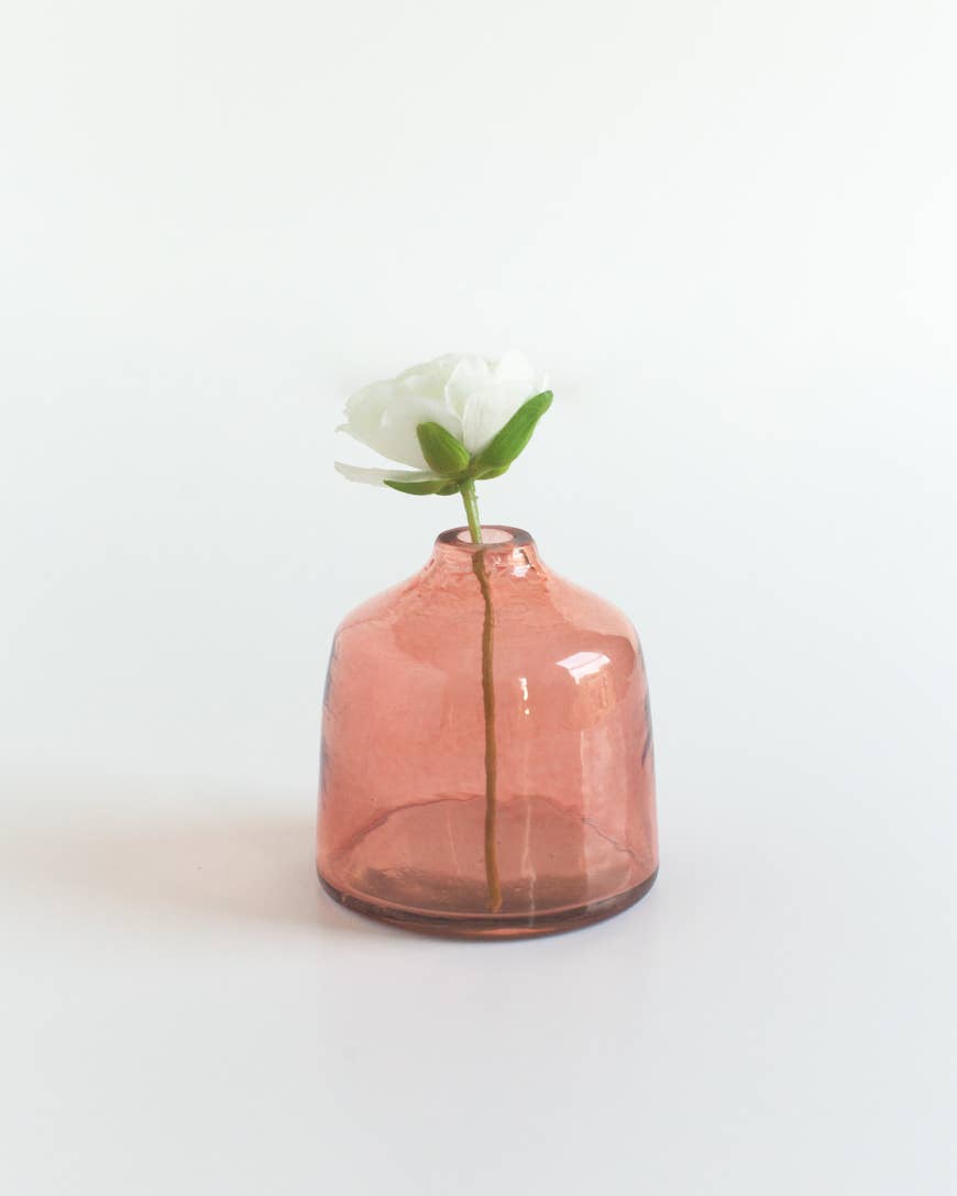 A single white flower with green leaves in the Bella Handblown Hammered Glass Bud Vase: Blush by Creative Women, set against a plain white background.