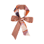 The Silk Skinny Scarf - Clay by Lost Pattern NYC is a double-sided silk satin piece with geometric patterns in orange, purple, and pink—perfect as a chic hair accessory or tied in a bow against a white background.